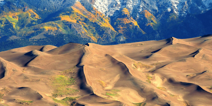 Snow-capped mountains with massive mountainous sand dunes below.