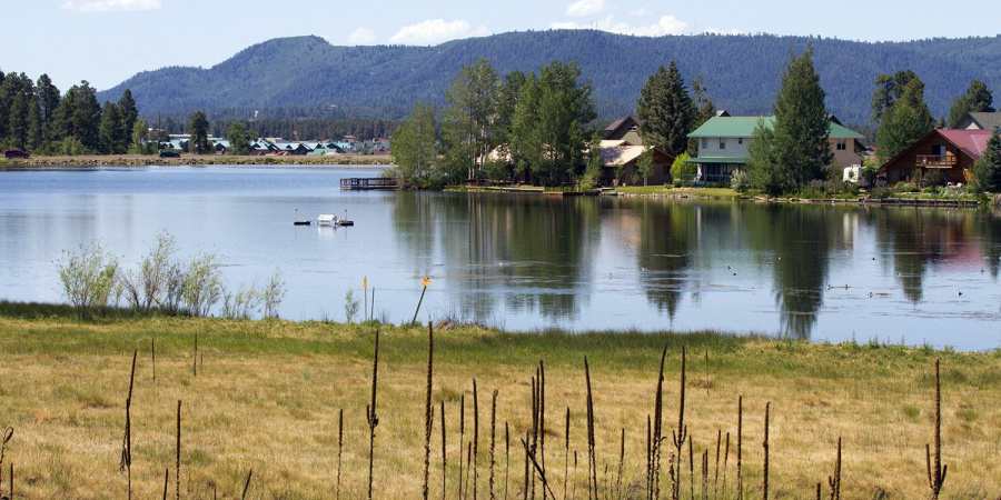 Pagosa Lake with reeds in the foreground with mountains and houses in the distance.