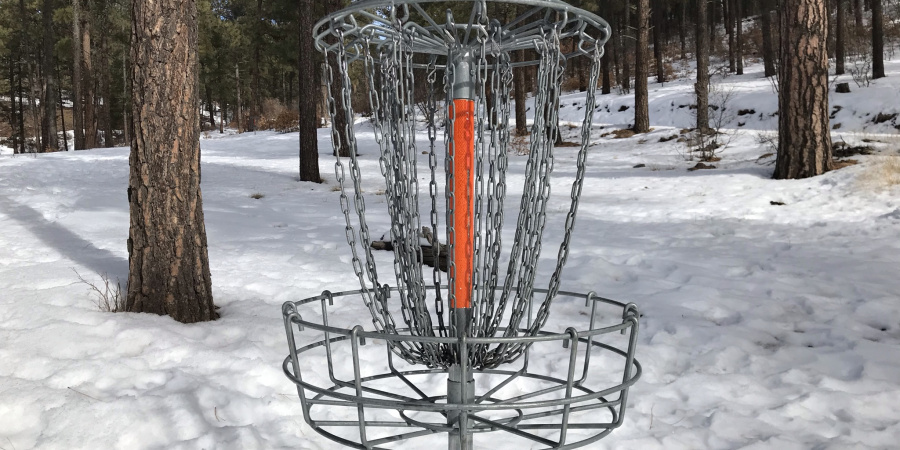 Reservoir Hill Disc Golf Basket amid snow & pine trees.