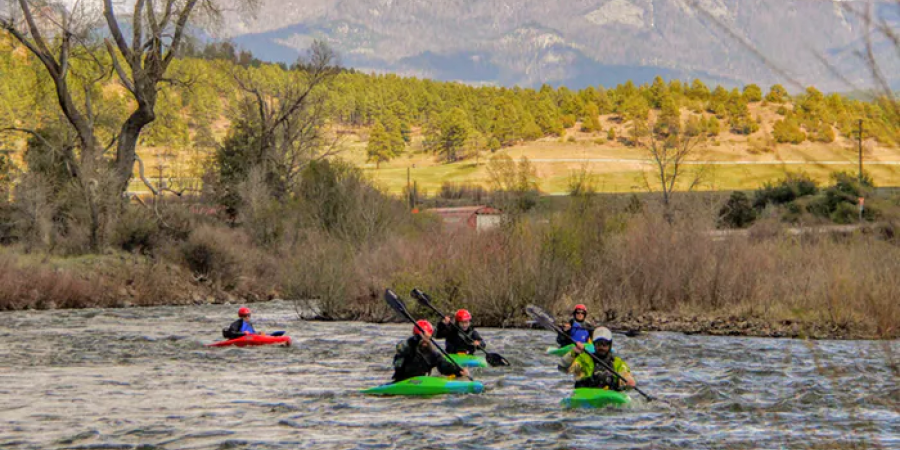 Kayakers on San Juan River with mountains in the background.